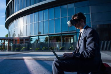 Bir dizüstü bilgisayar ve sanal gerçeklik gözlük kullanarak iş adamı