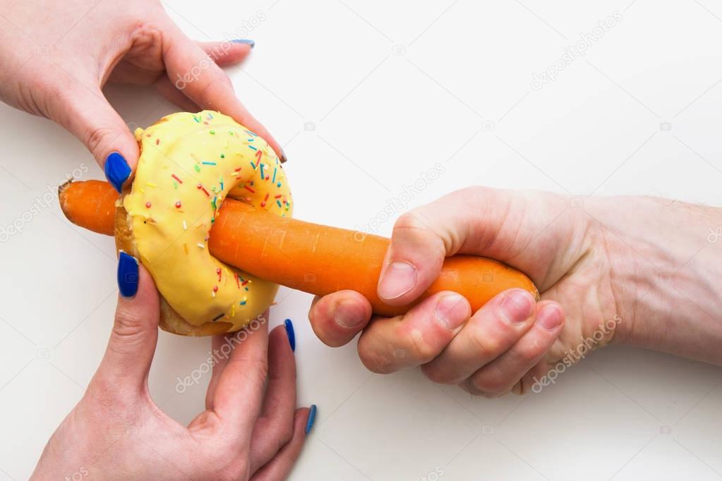 Hands with carrot inside donut hole. Symbol of sex