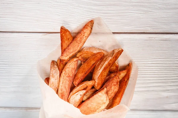Fresh fried potato wedges in paper on white table — Stock Photo, Image