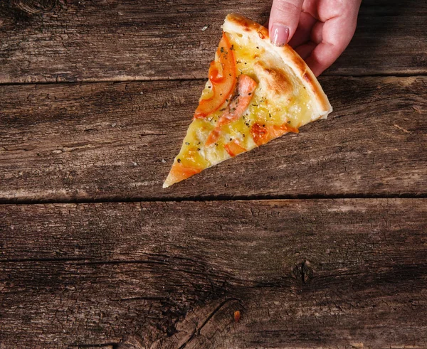 Slice of pizza in hand on dark wooden background