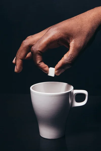 El hombre negro sostiene el cubo de azúcar por encima de la taza blanca — Foto de Stock