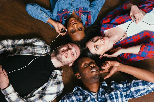 Cuatro amigos escuchan música juntos, yacen en el suelo — Foto de Stock