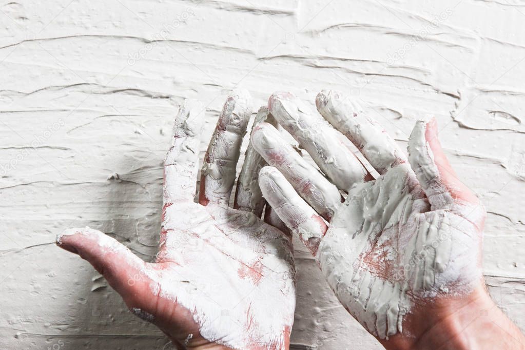 Builder hands in wet white plaster on stucco wall