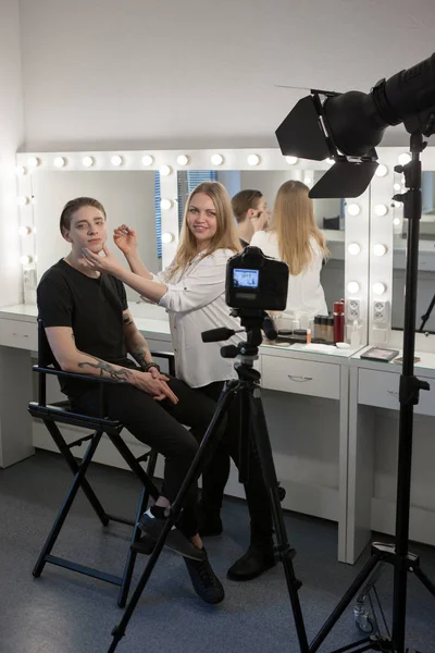 Smiling beautician woman applying male makeup