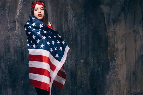 Girl wrapped in american flag on dark background — Stok Foto