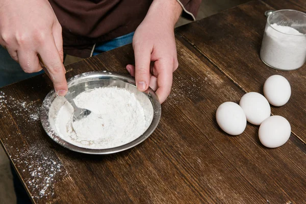 Chief mixes flour with eggs in bowl on table