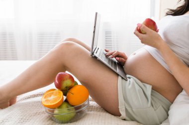 Hamile kadın içinde laptop sohbet sırasında elma yiyor