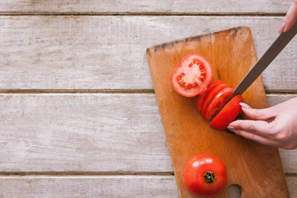 Женщина режет красные помидоры на деревянном столе — стоковое фото