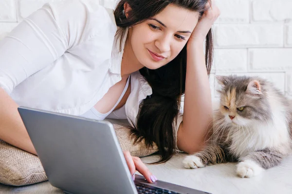 Молода жінка зі своєю кішкою дивиться на smth в ноутбуці — стокове фото