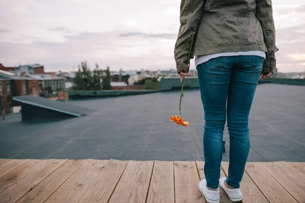 Mujer joven que se queda atrás con la flor naranja — Foto de Stock