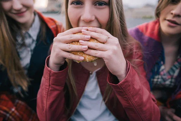 Młoda dziewczyna hot-eyed zjada burger, z bliska — Zdjęcie stockowe