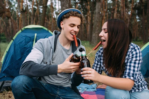 Para jeść kiełbaski i napoje piwa w pobliżu ognisko — Zdjęcie stockowe