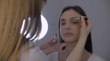 Makyöz çalışır, profesyonel makyaj yapar, kaşlar. Örnek bir kızın güzel yüzü. Makyaj sanatçısı genç bir kadına şık bir makyaj yapıyor. Yakın plan.