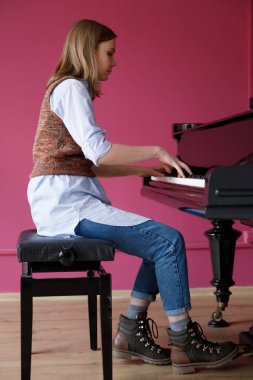A girl pianist plays the piano. Blonde on a pink background is engaged in music on the piano at home