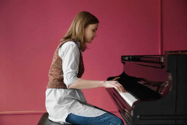 A girl pianist plays the piano. Blonde on a pink background is engaged in music on the piano at home — Stockfoto