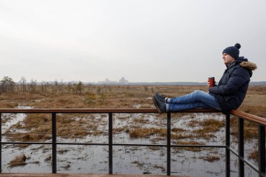 Doğada bir adam oturur, ufka bakar ve kahve içer..