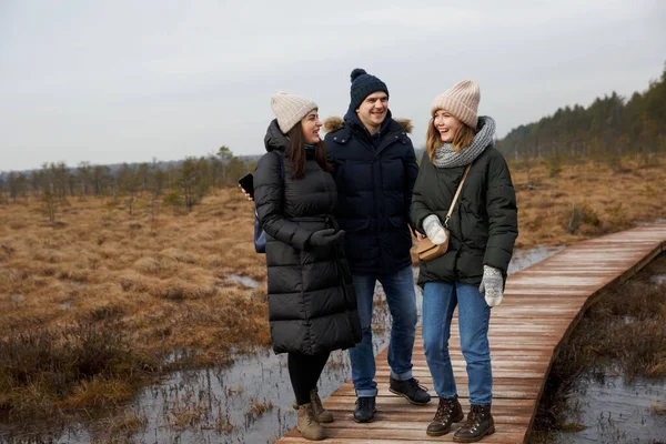 Egy fiú és két lány sétál a természetben. A barátok nevetnek és mosolyognak — Stock Fotó