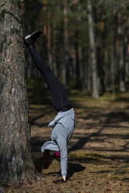 Ellerinin üzerinde duran, doğadaki bir kız sporla meşgul. Spor salonu yerine çam ormanı.