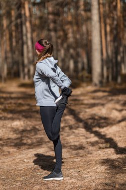 Kız egzersiz yapmadan önce ısınıyor. Çam ormanında koşuyor.