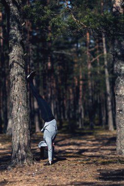 Ellerinin üzerinde duran, doğadaki bir kız sporla meşgul. Spor salonu yerine çam ormanı.
