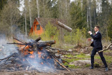 Adamın biri ateşe odun atıyor. Kulübeyi temizlemek, çöpleri yakmak. Takım elbiseli bir işadamı ülkede elleriyle çalışır..