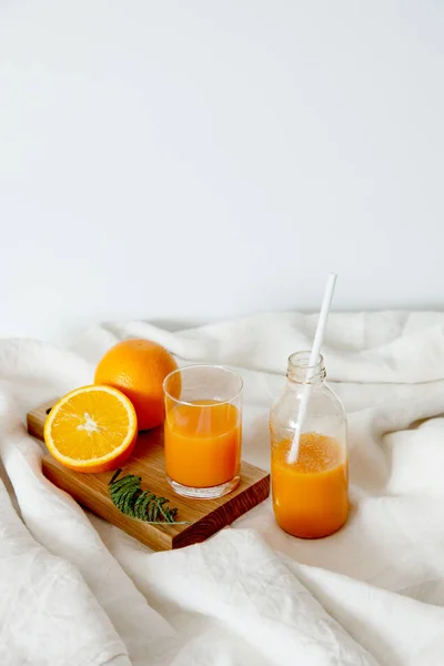 Naranja fresca para el desayuno en un vaso y en una botella con una pajita. Sobre el tablero de madera yace una naranja y una revista . —  Fotos de Stock