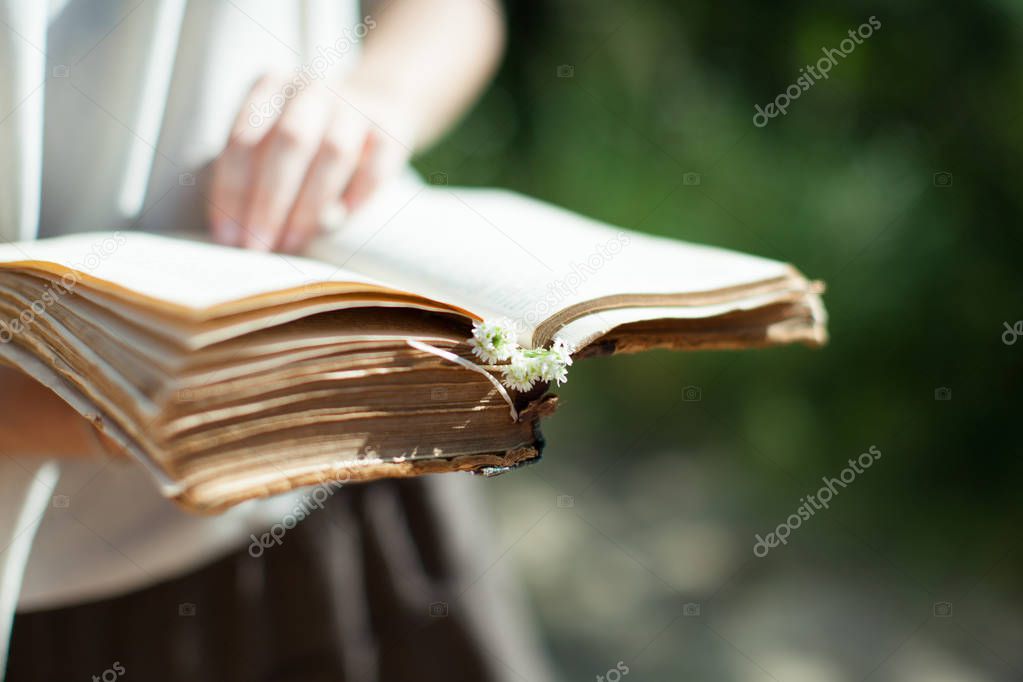 A young girl is holding a very old shabby book in her hands. Sum