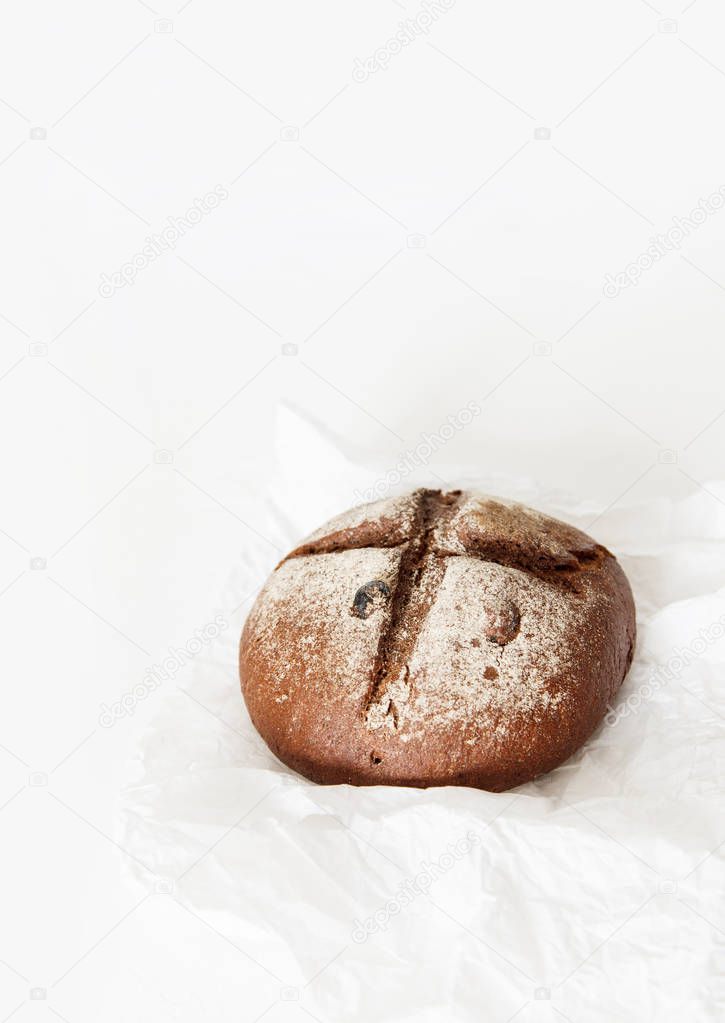 Round black bread lies on crumpled white paper on a white backgr