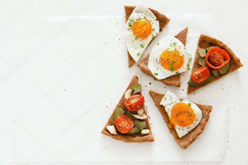 Slices of pie similar to pizza with vegetables, egg and avocado lie on white background, top view.