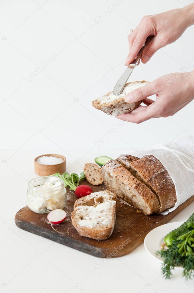 Bread with salt, butter, cucumber and radishes lie on a white background. A girl is buttering a sandwich.