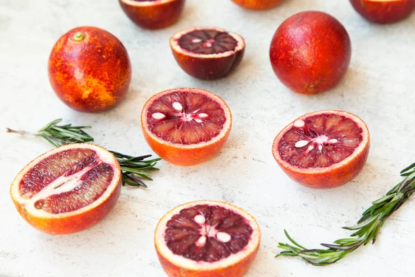 Red Sicilian orange whole and cut on a light background with branches of rosemary. Daylight, open space for your text.