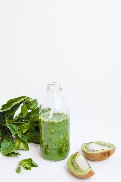 Зеленый коктейль в бутылке и в стакане со шпинатом, мятой, кемари, киви и яблоком на светлом фоне . — стоковое фото