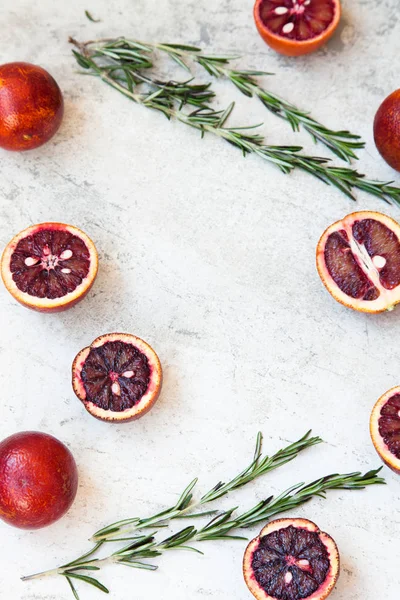 Naranja siciliano rojo entero y cortado sobre un fondo claro con ramas de romero. Luz del día, espacio abierto para su texto . — Foto de Stock