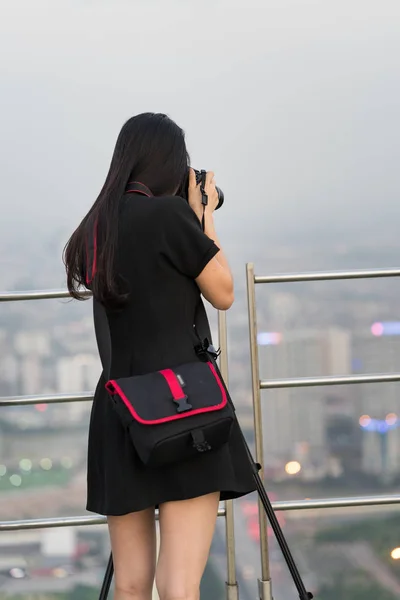 Closeup back view of female photographer taking photo of aerial cityscape from top of high building. Concept of woman, female photographer