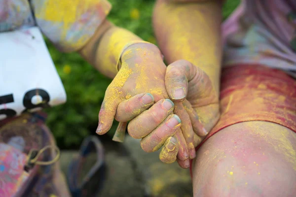 Hand with colorful powder holding other hand at color run event. Outdoor activity.