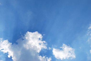 Mavi gökyüzündeki bulutların arasından geçen güneş ışınları