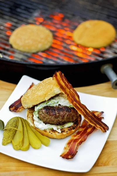 Barbecued hamburger with bacon and gherkin — Stock Photo, Image