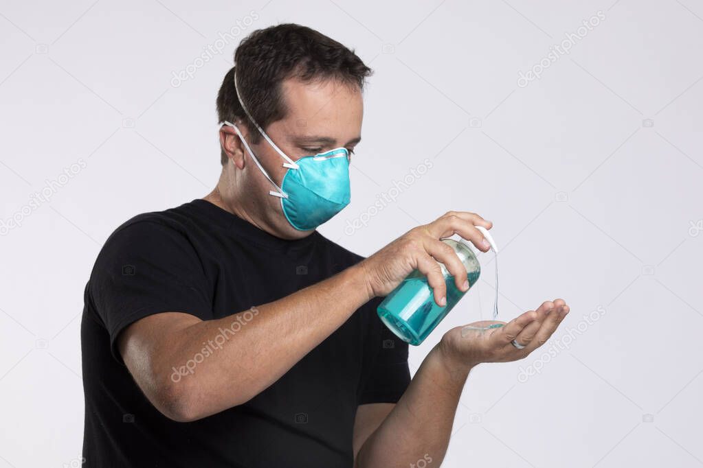 Man in a surgical mask squirting hand sanitizer or soap into his hand.