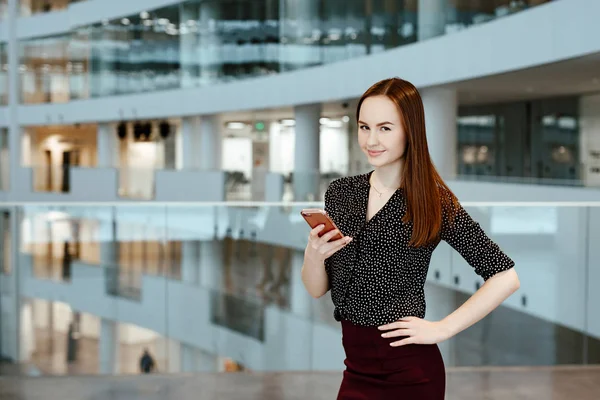 The young business woman talks on the smartphone against the background of office.