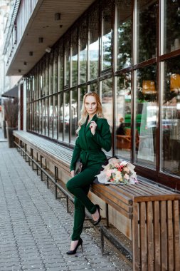 Sokak tarzı. Bir buket çiçek city café arka planı yeşil elbiseli sarışın güzel genç kadın portresi.