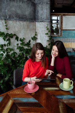 Toplantı kafede kız. Kızlar iletişim kurmak ve bir fincan kahve arkasında haberleri tartışmak. Kadın tablet bilgi izleyin.