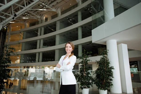 Business a portrait of the positive woman of the blonde in a white jacket against the background of modern office of business center.