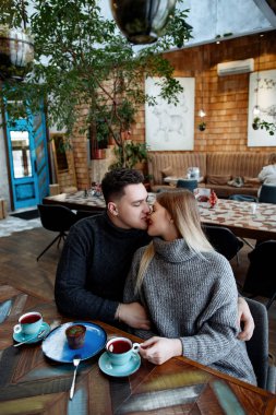 Genç güzel sevgi dolu çift kafede. Adam ve kadın rahat gri kazak iletişim, kucaklamak ve gülümse.