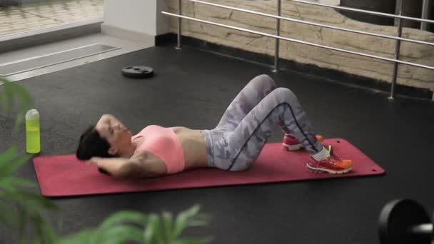 Frau auf Matte trainiert und drückt im Fitnessstudio vorsichtig auf den Bauch.
