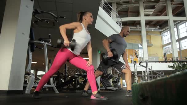 The sportswoman does curling a dumbbell with the male colleague in the big modern gym — Stock Footage The sportswoman does curling a dumbbell with the male colleague in the big modern gym Stock Footage