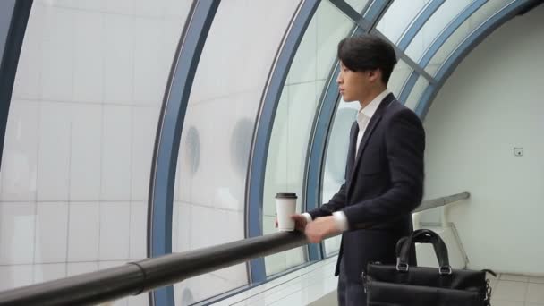 Male Asian man in jacket drinks coffee and looks at window on ra Male Asian man in jacket drinks coffee and looks at window on rain. Royalty Free Stock Footage