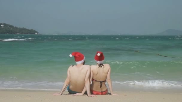 Milující pár v Santas klobouky sedí na pláži jižní pláže.