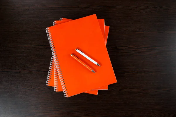 Orange Notebooks Lying Dark Brown Wooden Table Orange White Pens — Stock Photo, Image