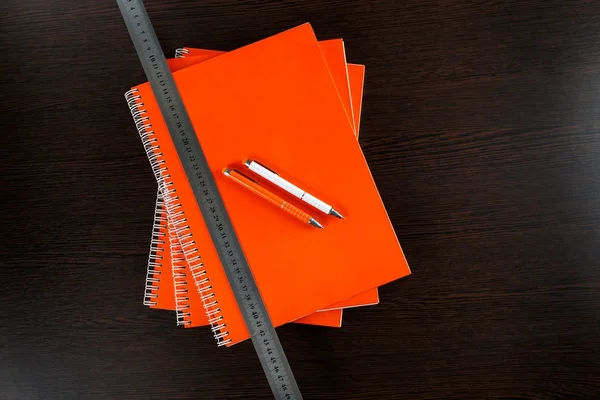 白いスケッチ ブックとオレンジ ノートをオレンジと白ペンで暗い茶色の木製のテーブルの上に横たわるとテープを測定 — ストック写真