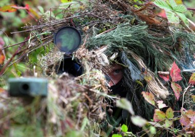Kamuflaj Avcısı ya da sonbahar kamuflaj arka planında çalılıklarda saklanan asker. Tüfekli keskin nişancı.